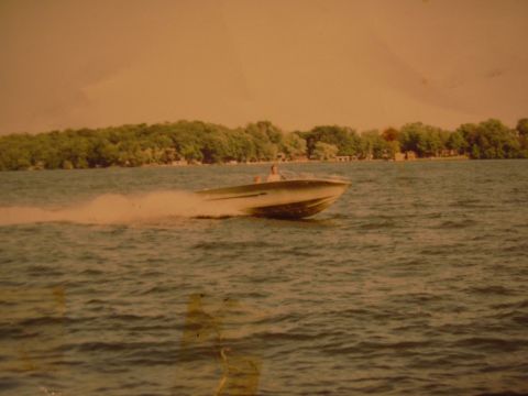 1977 Ford F-150 - A boat speeds across the water, leaving a wake behind it. The shoreline is visible in the background.
