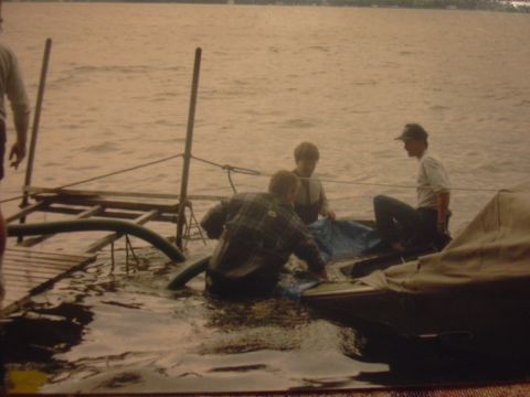 1977 Ford F-150 - Three individuals are on a boat that appears to be taking on water, with a dock and water in the background.