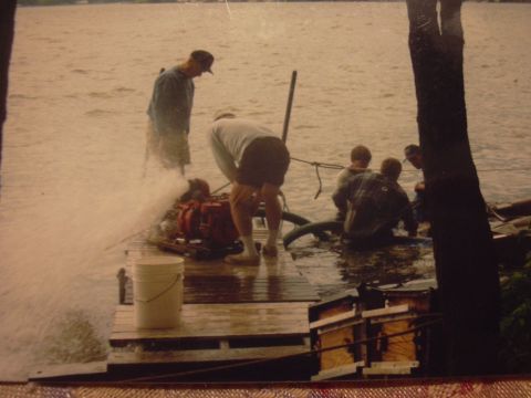 1977 Ford F-150 - People are gathered around a red engine on a wet wooden dock, with water spraying from the engine.