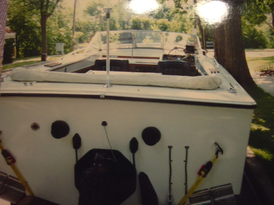 White boat with a tan interior and windshield, parked near trees