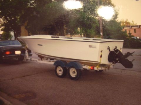 1977 Ford F-150 - A car tows a white boat on a trailer, with trees and buildings in the background.