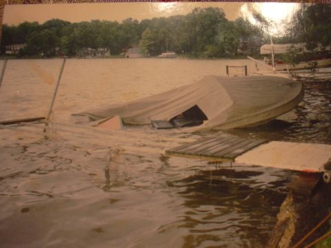 1977 Ford F-150 - A boat is partially submerged next to a wooden dock, with trees and houses visible in the background.