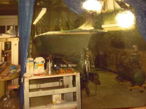 1977 Ford F-150 - A boat is covered by a tarp in a workshop setting, surrounded by tools and equipment.