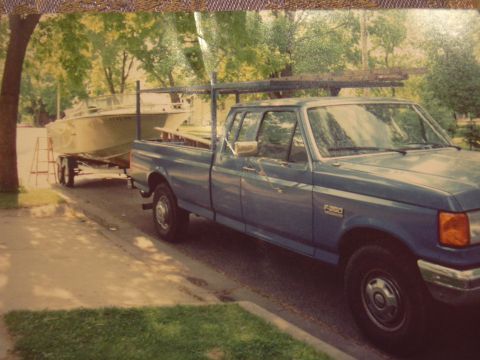 1977 Ford F-150 - A blue pickup truck tows a boat on a trailer down a residential street.