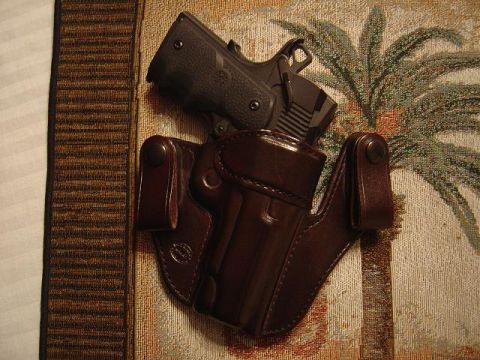1986 Ford Bronco II - A pistol rests in a brown leather holster, placed on a tapestry with a palm tree design. The image includes a watermark for SuperMotors.net.