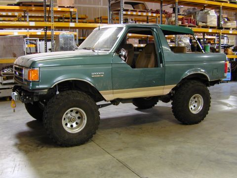 1989 Ford Bronco - This lifted Ford Bronco is parked inside a warehouse with storage shelves visible in the background.