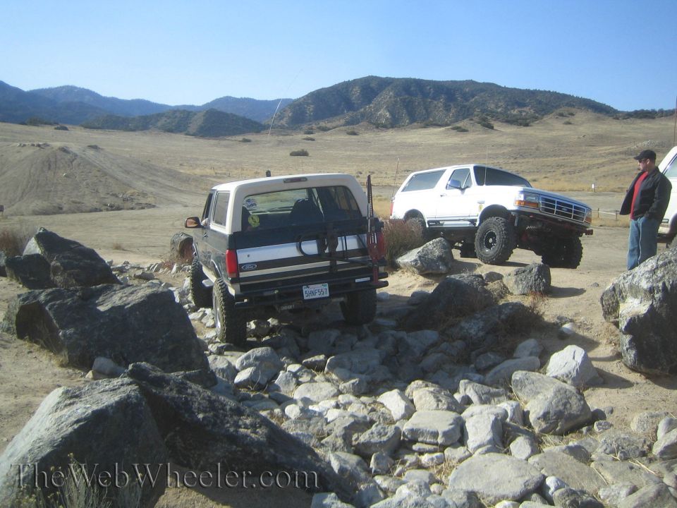 Two Ford Broncos off-roading over rocks, one black and tan, one white