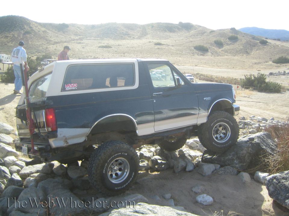 Ford Bronco with off-road tires climbing over rocks. MSD sticker visible on rear window