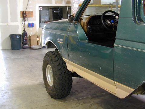 1989 Ford Bronco - Side view of a green 1989 Ford Bronco, a large off-road tire and tan lower body trim.