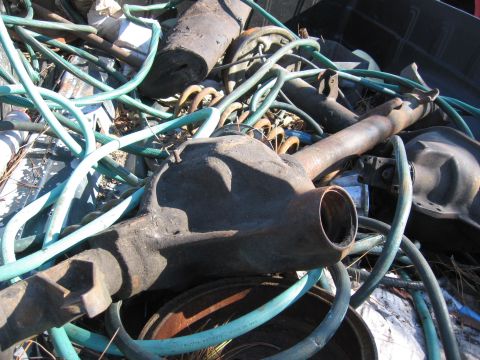 1974 Ford F-100 - A rusty rear axle assembly is piled with hoses and other scrap metal, suggesting it is destined for recycling or salvage.