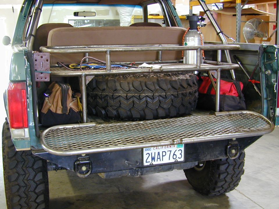 Custom tube cargo rack with spare tire, gear bags, and air tank in the back of a topless green Ford Bronco