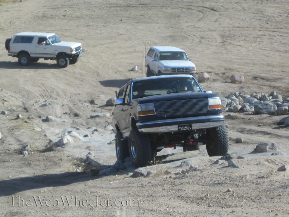 Black Ford Bronco with lifted suspension driving over rocks