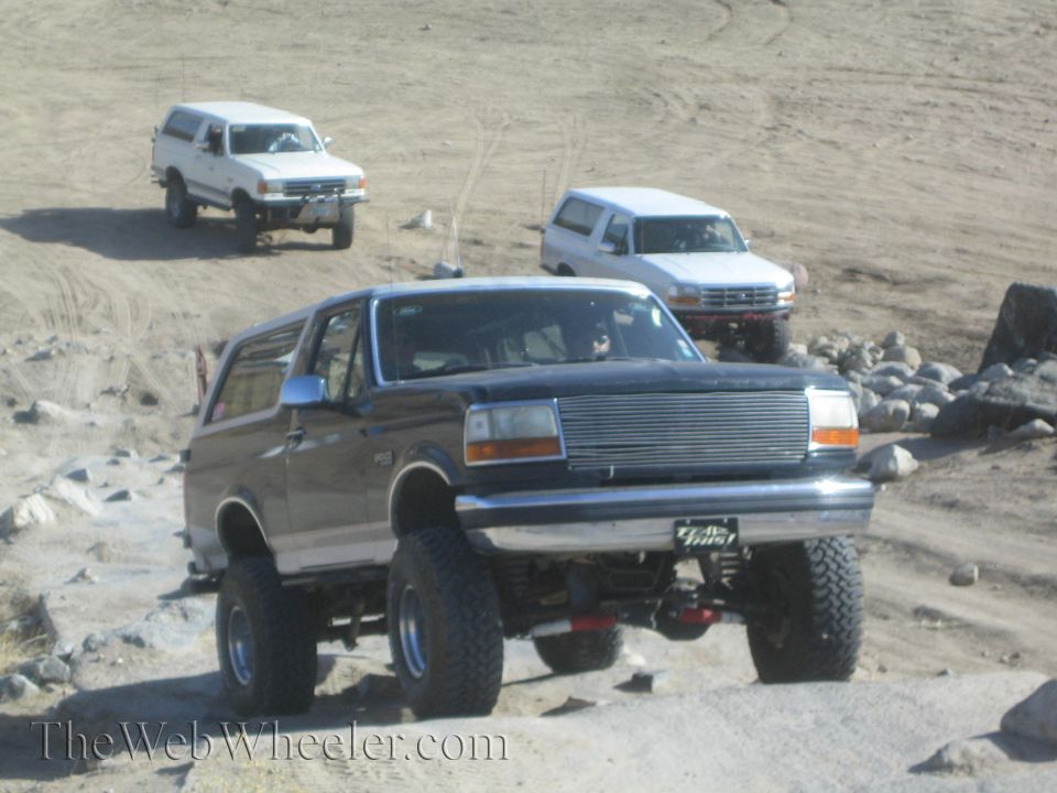 Dark SUV with chrome grille and large tires, two white SUVs in background
