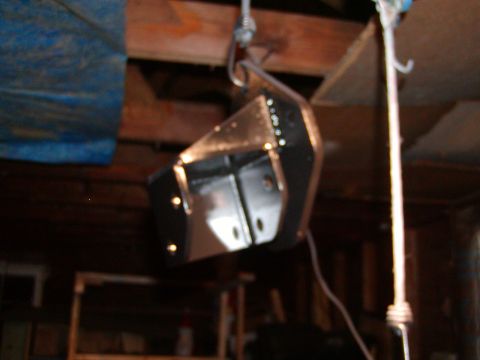 1991 Ford Bronco - A black metal suspension part is suspended from a hook in a workshop environment.