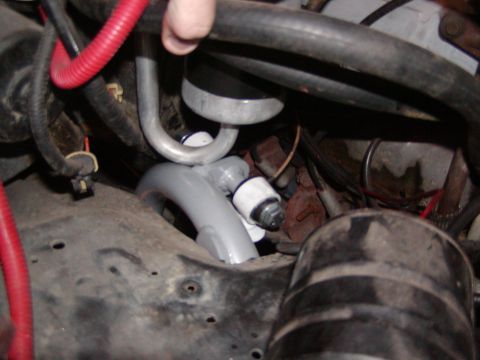 1991 Ford Bronco - Close-up view of engine bay components, including hoses and wiring, with a hand present.