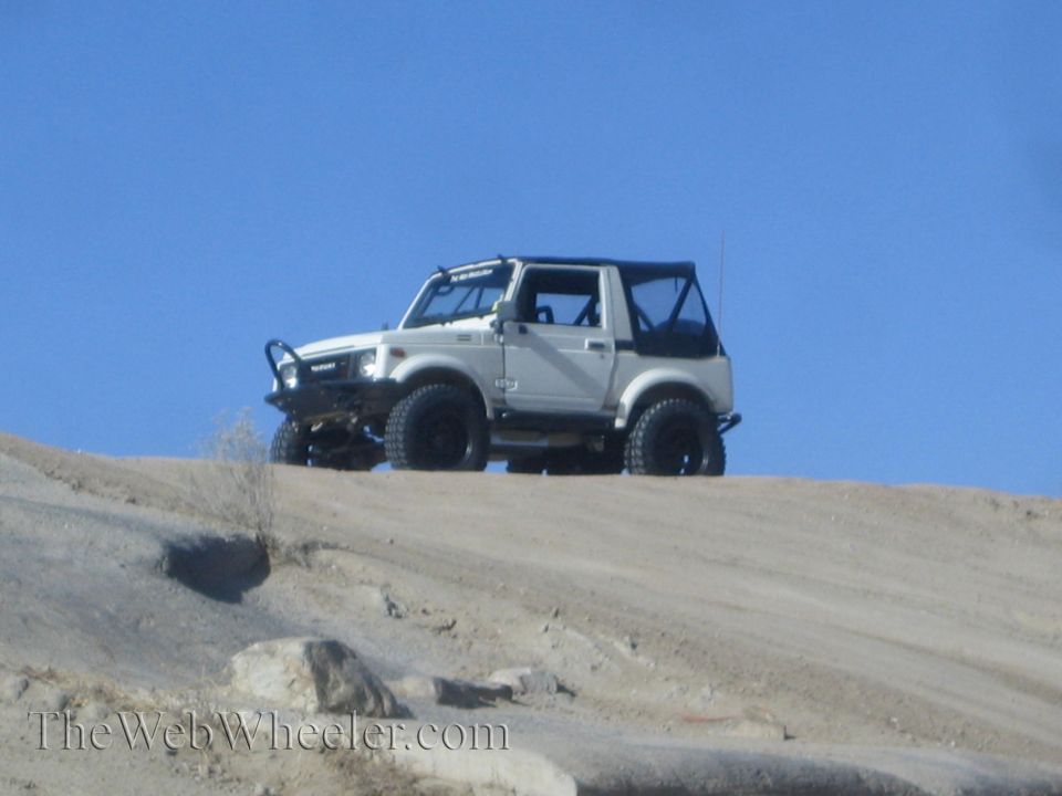 White 1987 Suzuki Samurai on a dirt hill under a clear blue sky