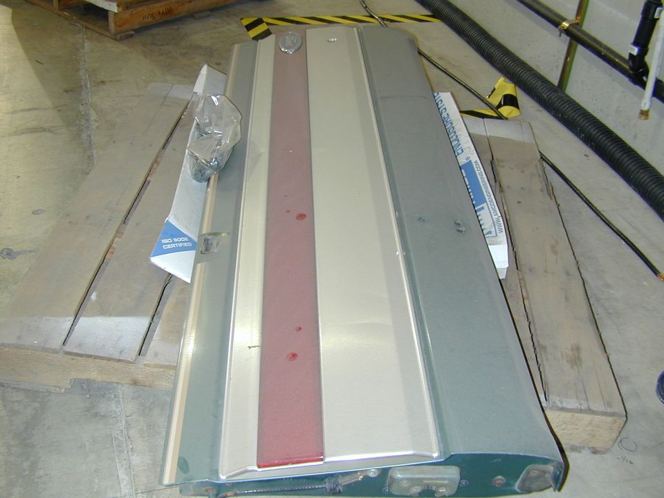 Silver car hood panel with a red stripe down the center, resting on wooden planks