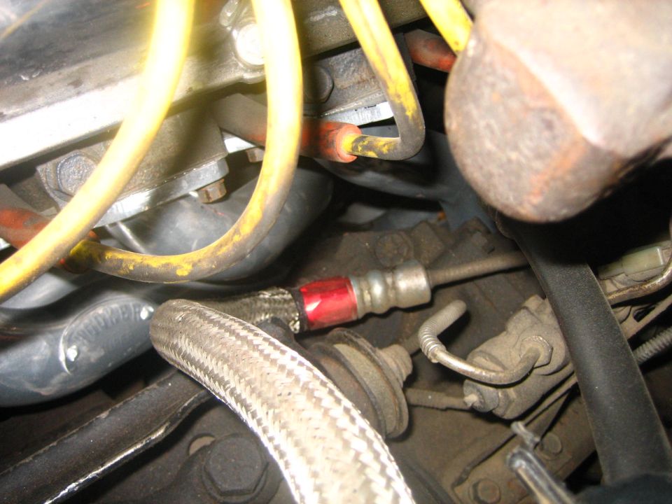 Engine bay with yellow spark plug wires, braided hose, and red-capped fitting
