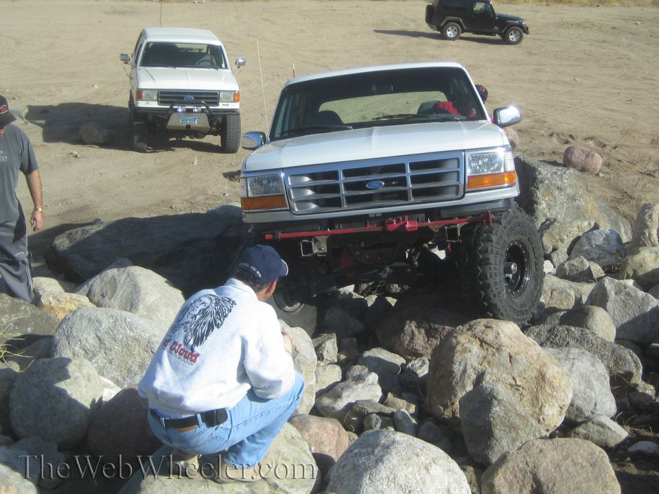 White Ford F-150 truck on rocks, another white truck and black Jeep in background
