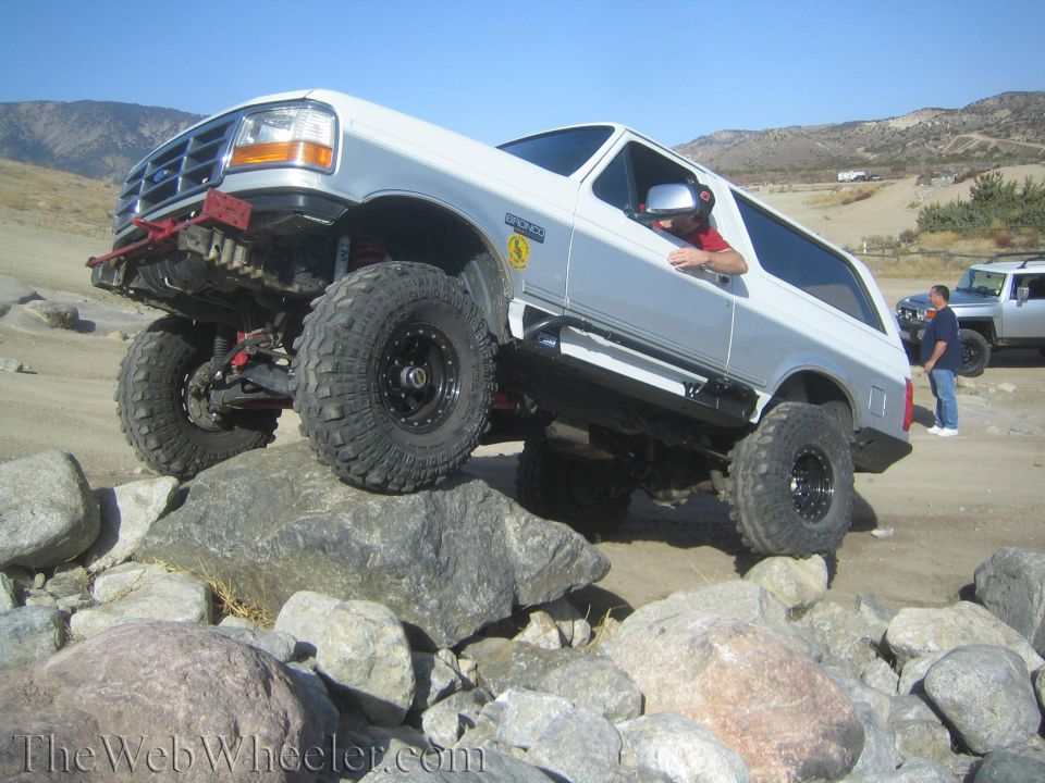 White and silver Ford Bronco with off-road tires climbing over rocks