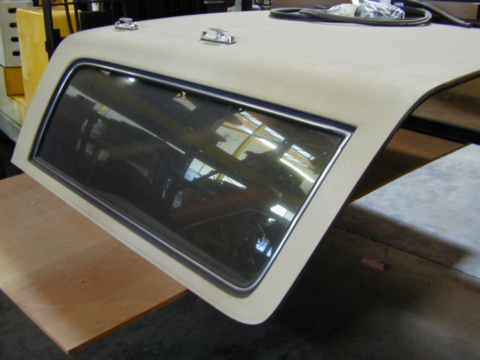 Vehicle hardtop with a side window, resting on a wooden surface. A yellow forklift is visible in the background