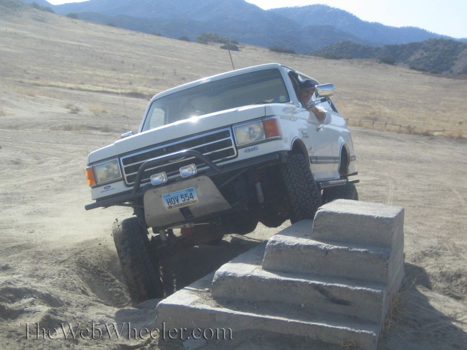 White Ford Bronco climbing over concrete steps off-road. License plate HOV 554