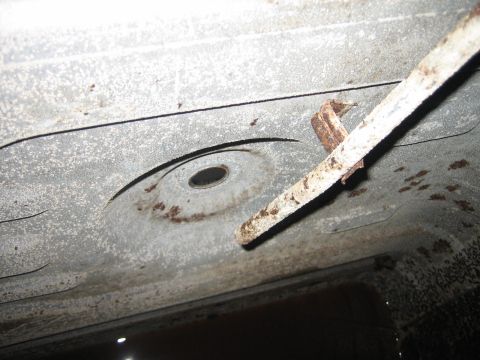 1976 Ford Ranchero - The underside of a vehicle reveals a rusty metal strap and a circular indentation, with visible text at the bottom right.