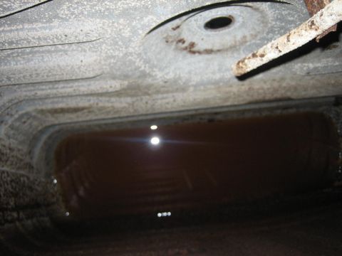 1976 Ford Ranchero - The underside of a vehicle reveals a gas tank filled with a dark liquid, showing signs of rust.