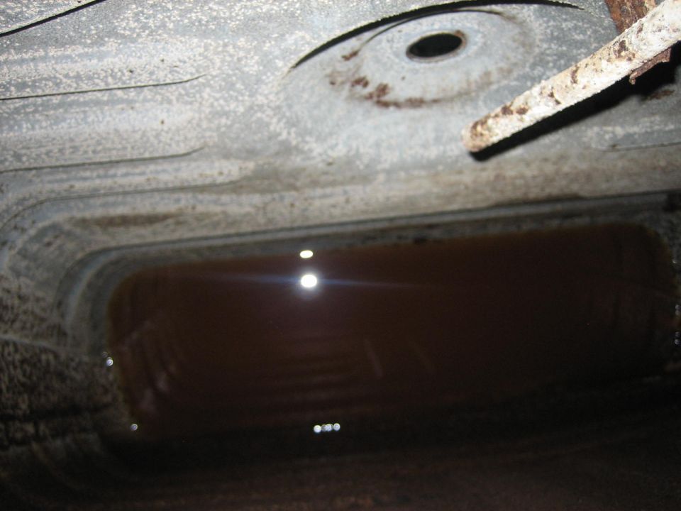 Underside of a vehicle showing a partially filled gas tank with rust and debris