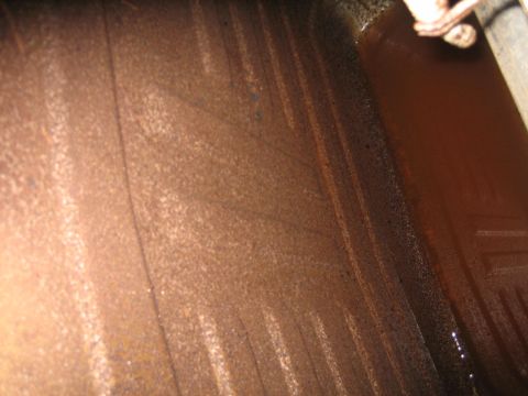 1976 Ford Ranchero - Close-up view of the interior of a rusty gas tank, showing textured surfaces and some dark liquid residue.
