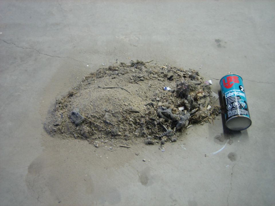 Pile of dirt and debris on concrete floor next to a can of lubricant