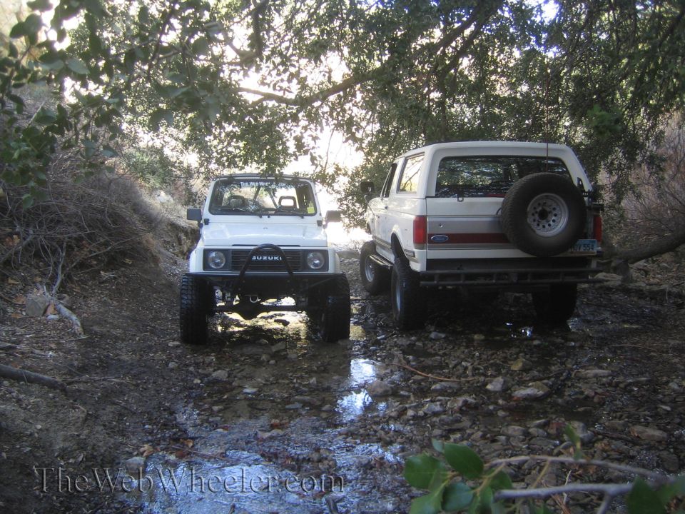White 1987 Suzuki Samurai front view with a Ford Bronco behind it on a dirt path