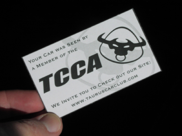 Hand holding a TCCA Taurus Car Club business card with a bull-head logo