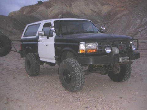1991 Ford Bronco - This modified Ford Bronco is parked in a desert landscape with hills in the background.