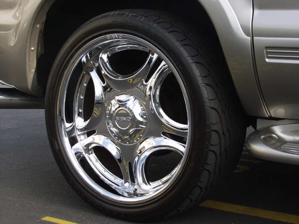 Chrome five-spoke wheel with OASIS tire on a silver SUV in a parking lot