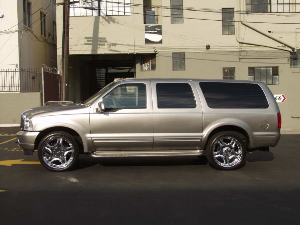 Silver Ford Excursion SUV in side profile on chrome wheels, parked in an alley