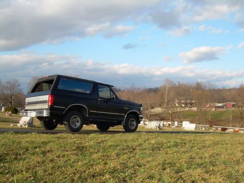 1992 Ford Bronco - This 1992 Ford Bronco is seen from a 3/4 front angle, parked on a grassy incline under a partly cloudy sky.