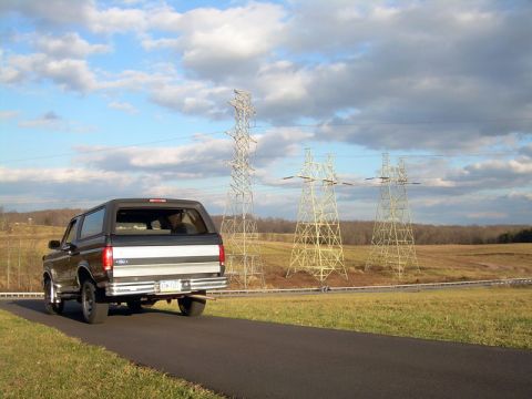 1992 Ford Bronco - 1992 Ford Bronco seen from the rear on a road with power line towers in the distance.