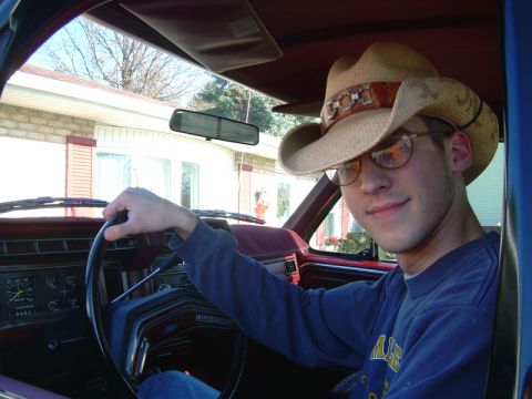 1984 Ford Bronco - Man in a cowboy hat smiles from the driver's seat of a 1984 Ford Bronco, with the dashboard and gauges visible.