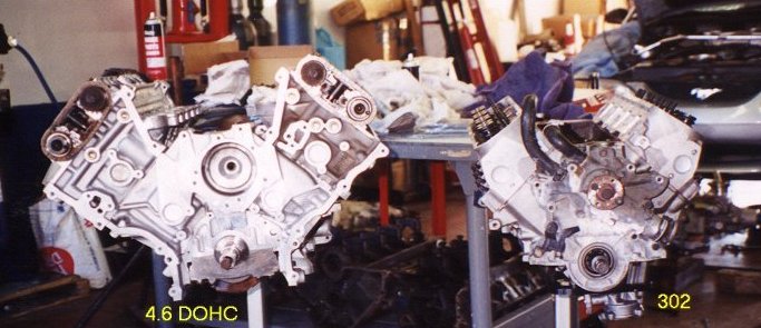 Two V8 engines, one labeled 4.6 DOHC, on a workbench with tools and parts in the background