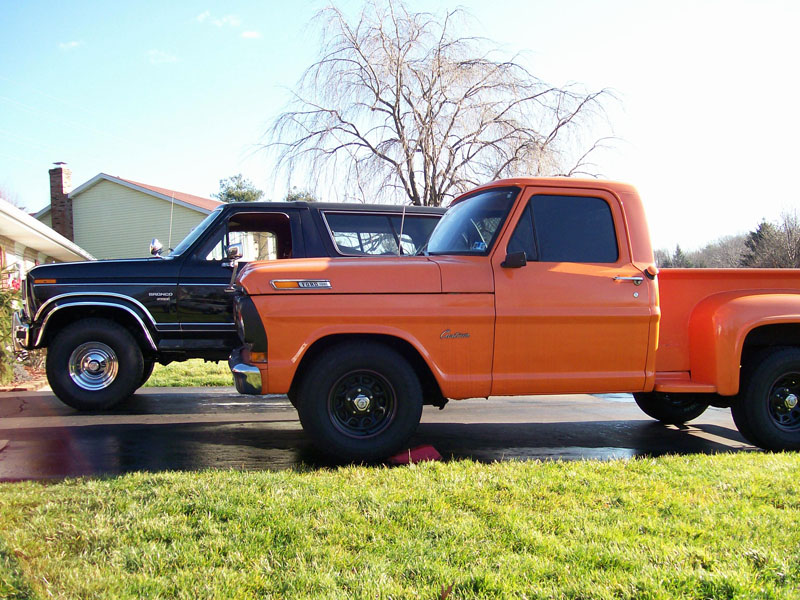 Orange vintage Ford stepside pickup beside a black Ford Bronco in a driveway