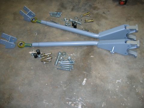 1992 Ford Mustang - A set of gray control arms and assorted hardware are displayed on a concrete surface.