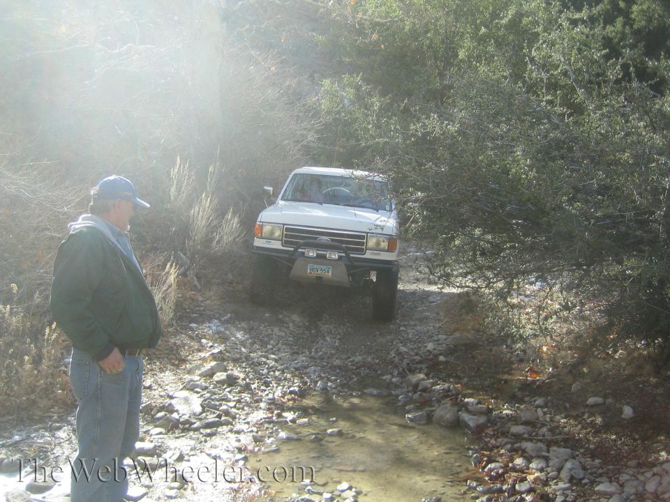 White SUV driving on a rocky trail with a man standing nearby. The SUV has a license plate that reads 'BGY-954'