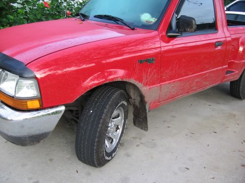 1974 Ford F-100 - A red Ford Ranger pickup truck is shown from the front quarter angle, with mud splattered on its body and fenders.