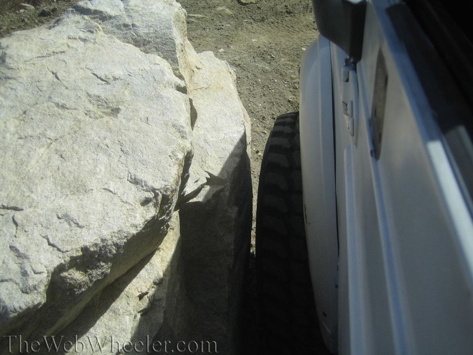 White vehicle's tire is very close to a large rock formation