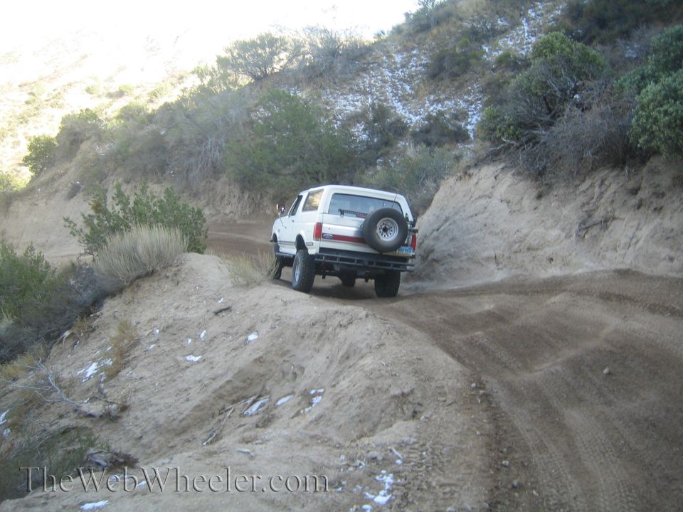 White SUV with spare tire on back driving on a dusty mountain road