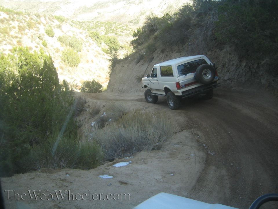 White SUV with spare tire on rear, driving on a dirt road in a canyon