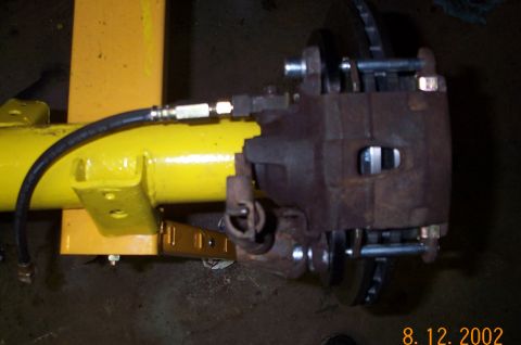 1986 Ford Bronco - Close-up of a rusty brake caliper and rotor assembly mounted on a yellow axle housing.