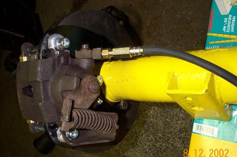 1986 Ford Bronco - Close-up of a disc brake caliper mounted to a rotor with an integrated parking-brake lever and coil return spring, plumbed with a braided f…