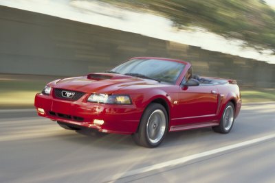 2003 Ford Mustang - A red 2003 Ford Mustang convertible is captured in motion on a highway.